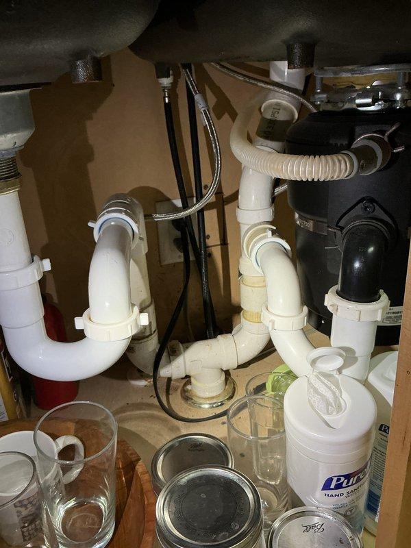 Responded to service call for multiple plumbing issues including leaking PVC drain line in basement and shower head replacement. Inspected under-sink plumbing configuration with white PVC P-trap assembly and garbage disposal connections, checking for proper drainage and seal integrity. Addressed basement plumbing concerns involving water heater or mechanical system connections with galvanized and copper piping. Completed repairs from customer's maintenance list, ensuring all connections were secure and leak-free.