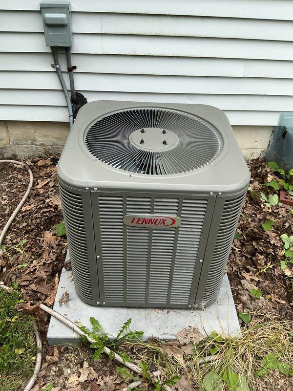 Responded to service call for Lennox air conditioning condenser unit experiencing water leakage from side panels and seams. Performed visual inspection of outdoor condenser unit and surrounding area, documenting unit condition and installation setup. Photographed equipment for service records showing unit placement on concrete pad with electrical disconnect properly mounted on exterior wall.
