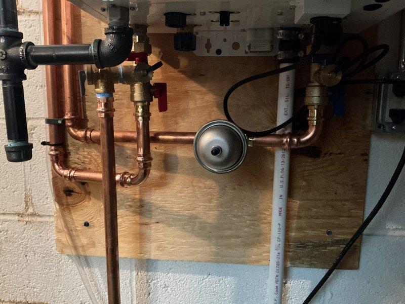 Replaced main water shut-off valve and installed Navien tankless water heater system. Coordinated with municipal water department for main water shut-off prior to commencing work. Installation included copper piping configuration with pressure gauge, red-handled isolation valves, PEX connections, and proper venting through exterior wall with white PVC pipe. Mounted complete system on plywood backing board for secure installation. Electrical outlet installation coordinated with licensed electrician to provide power supply for tankless unit. All components staged and core drilling completed for exterior venting requirements.