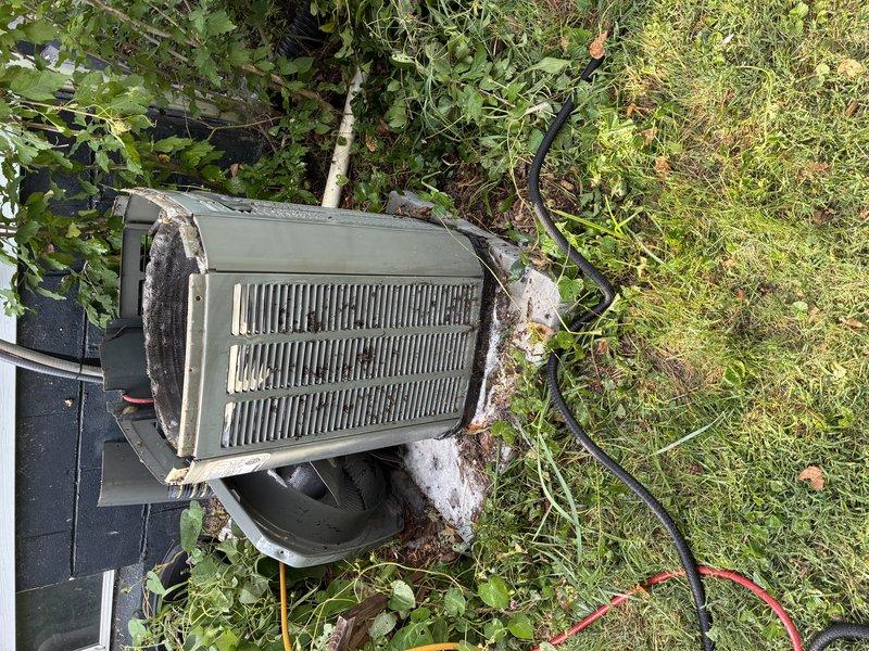 # HVAC Service Report

Responded to service call for 16-year-old central air conditioning system blowing room temperature air with no cooling. Upon arrival, discovered outdoor condenser unit had been completely displaced from its installation pad and was lying on its side in overgrown vegetation. Unit exhibited extensive physical damage, severe corrosion, deteriorated housing with protruding insulation material, and compromised refrigerant lines due to displacement and prolonged exposure to elements.

Assessed that the condenser unit sustained catastrophic damage rendering it beyond economical repair. Repositioned unit back onto concrete pad and documented extensive damage including dented housing, rusted components, and compromised electrical connections. Recommended complete system replacement due to age of equipment, extent of physical damage, and likelihood of refrigerant loss from damaged line sets.
