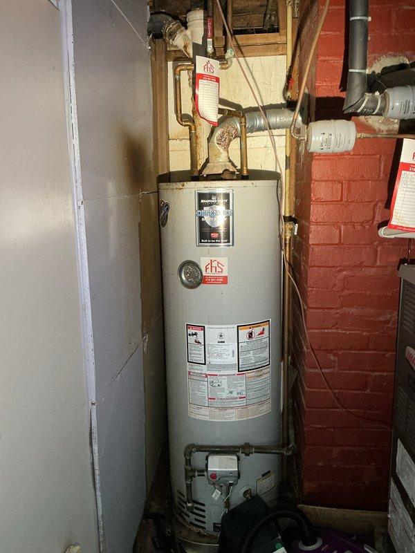 Completed free estimate for tanked water heater replacement. Inspected existing Bradford White Defender Safety System unit installed in basement utility area. Unit exhibited significant age-related deterioration including rust staining on top surface and around base, moisture staining on surrounding floor area, and general wear on tank exterior. Evaluated all plumbing connections including copper supply lines, PVC venting, brass fittings, and valve assemblies extending from top of unit. Assessed installation environment including exposed brick walls, wooden framing, and clearance requirements for replacement. Documented current water heater condition and configuration through photographs for estimate preparation. Accessed property using provided lockbox code at rear of residence.