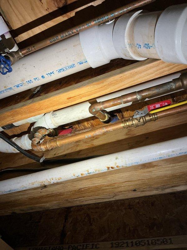 Responded to service call for dripping pipe between basement and main floor. Upon inspection, located source of water leak in exposed plumbing system within crawl space/basement ceiling area. Examined copper supply lines with brass fittings and PVC drain pipes running parallel to floor joists. Identified leak at pipe connection point and performed necessary repairs to stop active dripping. Verified all connections were secure and tested system to confirm leak was resolved.