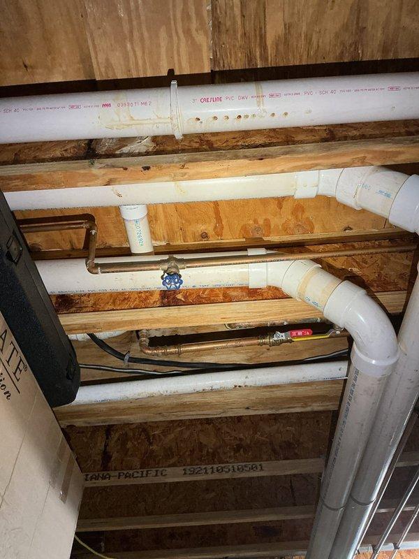 Responded to service call for dripping pipe between basement and main floor. Upon inspection, located source of water leak in exposed plumbing system within crawl space/basement ceiling area. Examined copper supply lines with brass fittings and PVC drain pipes running parallel to floor joists. Identified leak at pipe connection point and performed necessary repairs to stop active dripping. Verified all connections were secure and tested system to confirm leak was resolved.