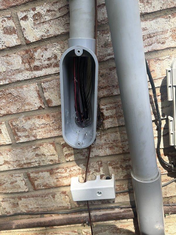 Removed existing 100 amp meter and deteriorated galvanized riser pipe from exterior brick wall, excavating as necessary for complete removal. Installed new PVC riser with expansion coupling and repositioned meter base lower on wall to accommodate existing service conductor length. Removed improperly terminated galvanized conduit from back of main panel, sealed penetration, and rerouted service entrance conductors through rim joist. Installed new grounding electrode system with ground rods, verified existing waterline and hot water tank grounding connections were code-compliant.