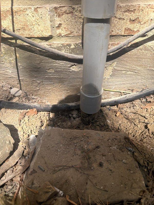 Removed existing 100 amp meter and deteriorated galvanized riser pipe from exterior brick wall, excavating as necessary for complete removal. Installed new PVC riser with expansion coupling and repositioned meter base lower on wall to accommodate existing service conductor length. Removed improperly terminated galvanized conduit from back of main panel, sealed penetration, and rerouted service entrance conductors through rim joist. Installed new grounding electrode system with ground rods, verified existing waterline and hot water tank grounding connections were code-compliant.