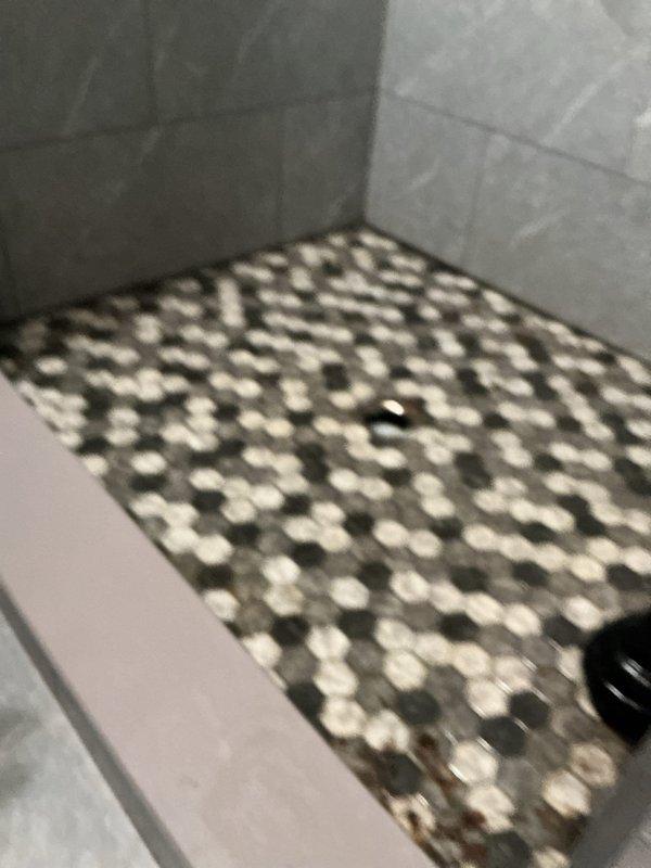 Responded to emergency main drain backup affecting bathroom fixtures with standing water approximately 3 inches deep on floor and sewage backup into shower. Upon arrival, confirmed improper toilet sizing for drainage system contributing to blockage that had persisted for 4-5 days. Performed main drain cleanout procedure to clear obstruction and restore proper flow through drainage system. Verified all fixtures draining properly after cleanout completion. Documented extensive water damage and staining to hexagonal tile flooring from prolonged sewage backup exposure.