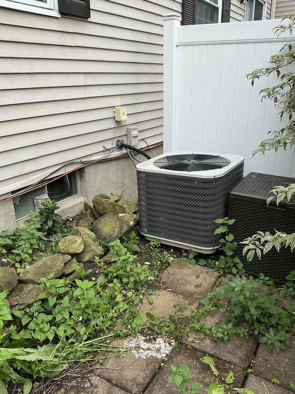 Conducted comprehensive on-site evaluation for complete HVAC system replacement at residential property. Assessed existing cylindrical outdoor condensing unit positioned on concrete pad with platform bases in side yard area, noting current equipment configuration and clearances relative to foundation, privacy fencing, and utility connections. Evaluated indoor air handler and furnace system located in basement mechanical room, documenting current beige cabinet unit alongside water heater, existing ductwork routing through floor joists, and electrical service connections. Photographed both exterior and interior equipment installations to document pre-replacement conditions and facilitate accurate equipment sizing and replacement planning for forthcoming system installation.