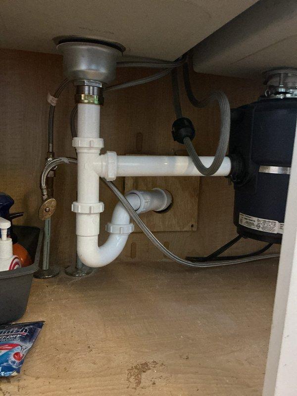 Addressed persistent kitchen drain clog that exceeded standard cable length by pulling dishwasher to access drain line, correcting improperly configured deep "U" trap, and replumbing basket strainer, P-trap, and drain arm assembly. Work included lowering drain arm for proper trap installation, attempting cable clearance from dishwasher access point, and preparing for potential ceiling access in basement if additional drain line replacement from stack connection to sink became necessary.