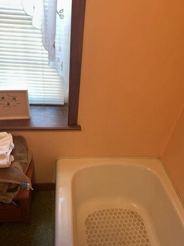 Converted existing bathtub to walk-in shower installation. Removed standard tub fixture, decorative wooden posts, and associated hardware from corner bathroom location. Prepared plumbing connections and drainage system for new shower configuration. Documented existing bathroom conditions including yellow-painted walls, wooden vanity, and speckled flooring prior to conversion work.