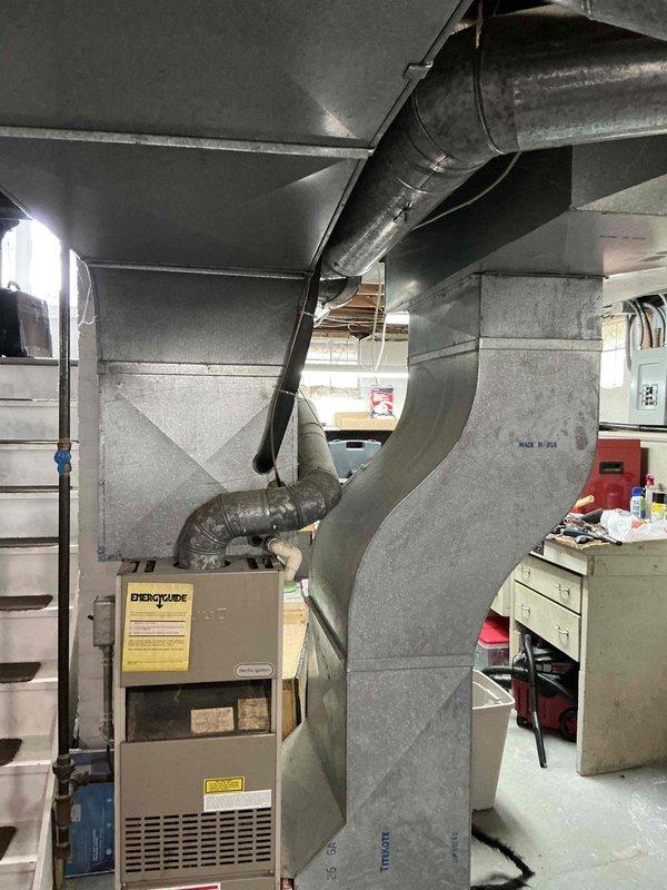 Conducted free replacement estimate for existing furnace and air conditioning system in residential property. Evaluated aging HVAC equipment located in unfinished basement utility area, including furnace unit with visible EnergyGuide labeling and associated ductwork system. Assessed condition of galvanized steel ductwork running from furnace unit along exposed ceiling joists. Documented existing system configuration through photographic documentation showing furnace installation against concrete block wall, metal supply ductwork, and basement mechanical room layout. Provided replacement recommendations and equipment options for both heating and cooling systems based on current installation conditions and space requirements.