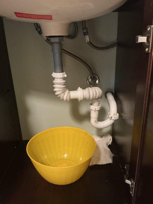 Responded to clogged bathroom sink in residential property. Upon arrival, assessed the undermount sink with bronze widespread faucet and dark wood vanity cabinet. Accessed the P-trap assembly beneath the sink and identified blockage in the drain line. Removed and disassembled the white PVC P-trap configuration, clearing accumulated debris and buildup causing the obstruction. Inspected flexible corrugated section and rigid plastic pipe segments for additional blockages. Cleaned all drain components thoroughly and reassembled the P-trap with proper slip-joint fittings to ensure watertight connections. Tested drain flow and verified proper drainage with no leaks detected at connection points. Left work area clean and plumbing system fully operational.