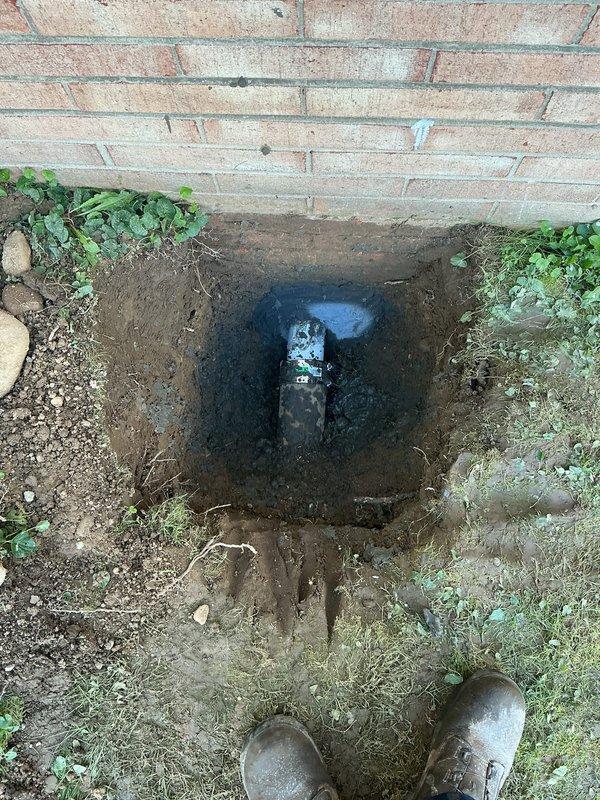 Excavated along exterior foundation wall to access deteriorated underground drainage system. Removed and replaced failed wye fitting and copper drain lines serving two bathroom groups and kitchen. Installed new drainage piping to restore proper wastewater flow from all affected fixtures. Backfilling arranged with separate contractor, with landscaping and grass restoration excluded from scope of work.