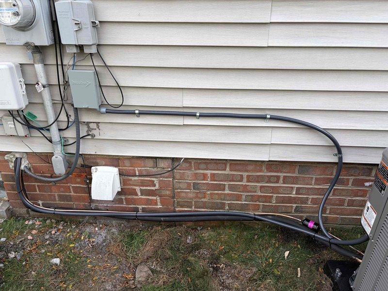 Completed full HVAC system installation consisting of an 80% efficiency furnace and air conditioning system. Installed new Lennox condenser unit on exterior pad with proper clearances from building structure, positioned on black plastic base pad with adequate airflow access on all sides. Routed refrigerant lines and electrical conduit from outdoor unit to interior furnace location, securing black electrical conduit along brick foundation using appropriate mounting clips and following building contours. Connected all electrical components including new meter connections, junction boxes, and service disconnect. Installed gray PVC and flexible metallic conduit for proper line protection and code compliance. Verified all electrical connections are secure and properly grounded. System tested and confirmed operational with proper airflow, refrigerant charge, and temperature differentials meeting manufacturer specifications.