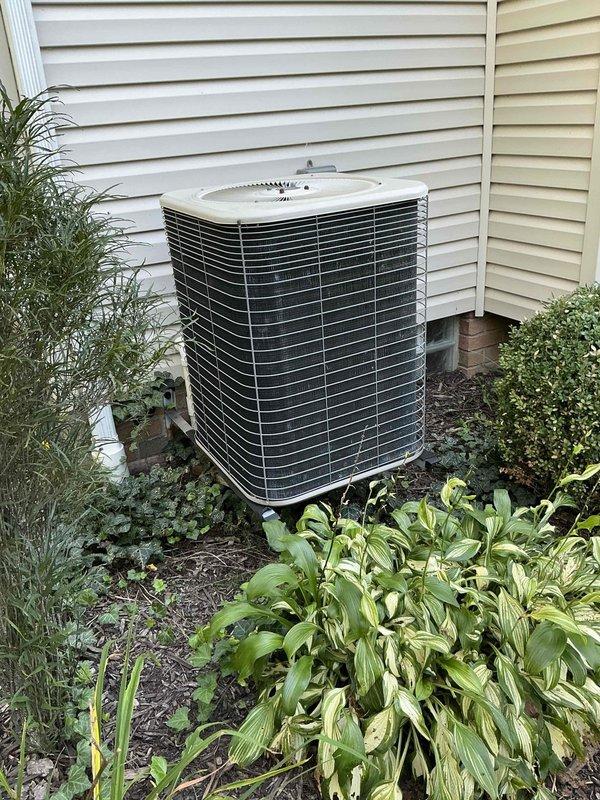Conducted comprehensive on-site evaluation for complete HVAC system replacement at residential property. Assessed existing outdoor air conditioning condenser unit positioned against exterior wall in landscaped area, documenting current equipment specifications, installation configuration, and surrounding site conditions. Photographed unit placement on concrete pad, electrical disconnect box mounting, refrigerant line routing, and clearance requirements relative to vegetation and structures. Evaluated system accessibility for future replacement installation, noting mulched garden bed with hostas and ornamental plantings requiring protection during equipment changeout. Reviewed electrical service connection and conduit pathways for compatibility with new equipment specifications. Provided detailed replacement options and equipment recommendations based on current system assessment and homeowner requirements.