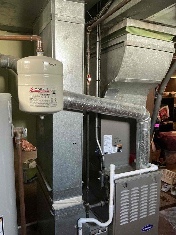 Completed furnace replacement estimate for 12-year-old unit with failed motor. Evaluated existing Carrier furnace system in basement utility area with associated ductwork, refrigerant lines, and condensate drainage. Documented current installation including vertical air handler configuration, insulated plenum, sheet metal distribution ductwork, and copper refrigerant piping for replacement quotation purposes.