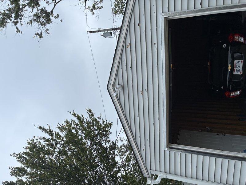 Replaced existing garage floodlight fixture with customer-provided dual-head LED motion sensor security light on exterior metal building. Removed old fixture, installed new mounting hardware, connected electrical wiring to the dual-head unit with central motion detector, and verified proper operation of both LED light heads and motion sensing functionality.