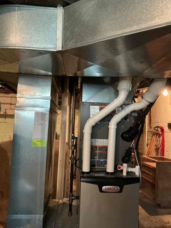 Responded to service call for moisture accumulation under furnace during air conditioning operation. Upon inspection, found condensate drainage issue from central air system affecting Lennox furnace installation. Examined PVC condensate drain lines, evaporator coil drainage, and surrounding equipment for proper operation. Verified condensate pump function, cleared any blockages in drain lines, and ensured proper pitch and routing of white PVC drainage piping extending from unit. Inspected furnace base and surrounding floor area for moisture damage and confirmed source of water accumulation. Checked air handler and ductwork connections for secondary drain pan overflow or leakage. Tested system operation with air conditioning running to verify proper condensate removal and confirmed no further moisture issues at furnace base upon completion.