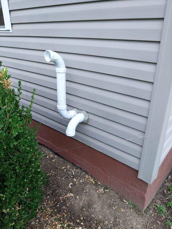 Conducted installation inspection of residential furnace system and identified code violation with exhaust venting materials. The cellular core PVC piping currently installed for the furnace exhaust vent does not meet manufacturer specifications and approval requirements. Documented the non-compliant venting configuration with photographs showing both exterior termination point and interior mechanical room installation. The white PVC vent pipe assembly extends from the furnace unit through the foundation wall with multiple 90-degree elbows terminating on the exterior gray vinyl siding. Installation has been placed on hold pending manager review and approval for corrective action to bring the system into compliance with manufacturer requirements and applicable codes.