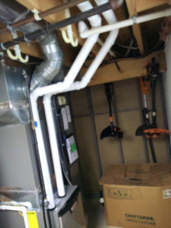 Conducted installation inspection of residential furnace system and identified code violation with exhaust venting materials. The cellular core PVC piping currently installed for the furnace exhaust vent does not meet manufacturer specifications and approval requirements. Documented the non-compliant venting configuration with photographs showing both exterior termination point and interior mechanical room installation. The white PVC vent pipe assembly extends from the furnace unit through the foundation wall with multiple 90-degree elbows terminating on the exterior gray vinyl siding. Installation has been placed on hold pending manager review and approval for corrective action to bring the system into compliance with manufacturer requirements and applicable codes.