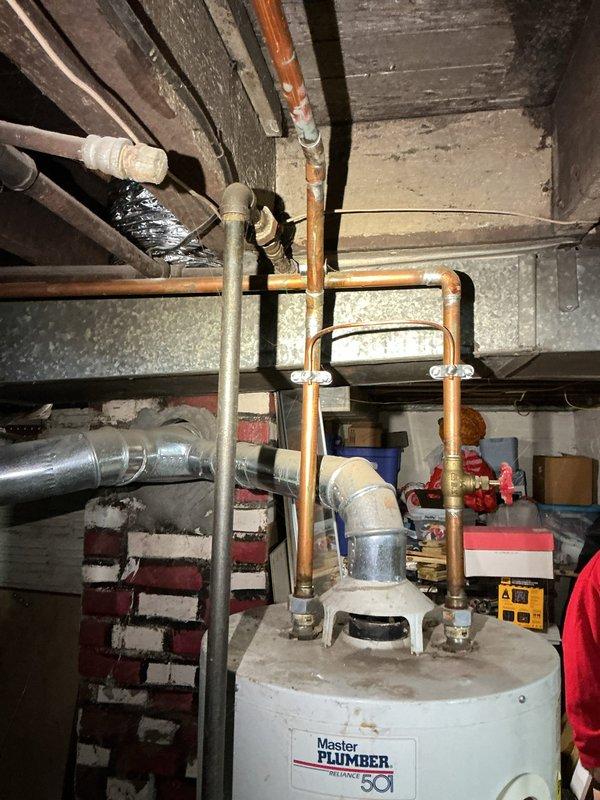 Provided complimentary assessment and quote for replacement of 25-year-old tanked water heater located in basement utility area. Upon inspection, evaluated existing Master Plumber brand water heater with connected copper piping, pressure relief valve system, and associated shut-off valves. Assessed current installation configuration including top-mounted plumbing connections with U-shaped copper pipe routing and red-handled isolation valve. Documented existing plumbing infrastructure, support pole positioning, and available workspace for potential replacement unit installation. Friends and family discount applied to quoted replacement services.