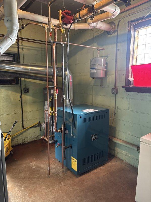 Completed installation of new hot water boiler system in basement mechanical room. Installed blue residential boiler unit with associated copper piping, valves, and connections to existing overhead plumbing infrastructure. Connected expansion tank, configured supply and return lines with isolation valves, and integrated system with existing ductwork. Installed code-compliant smoke detector in mechanical room area. All components tested and verified operational upon completion.