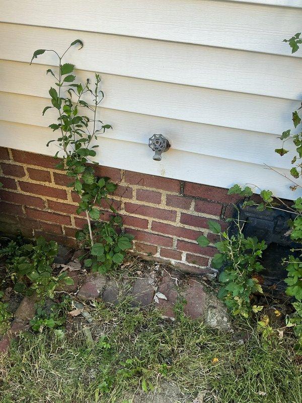 Responded to service call addressing multiple plumbing concerns including a stuck hose fitting on exterior spigot, frequently clogging floor drain, and non-functioning water heater. Inspected outdoor spigot mounted on foundation where hose end was seized to the connection point. Assessed electrical panel and water heater system to diagnose heating failure. Documented site conditions with photographic evidence showing exterior spigot location on brick and vinyl siding foundation area, as well as electrical panel configuration for water heater troubleshooting purposes.