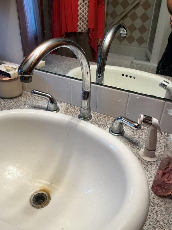 Responded to service call for non-operational sump pump and leaking faucets in kitchen and bathroom. Inspected sump pump system in basement utility area, verifying pump operation, discharge piping integrity, and electrical connections. Examined bathroom faucet fixture with dual-spout chrome design, assessing for leaks at handles, base connections, and supply lines. Documented existing conditions of plumbing fixtures including mineral buildup around drain areas and overall system functionality. Verified sump pump basin installation, submersible pump positioning, and vertical PVC discharge pipe secured to wall with proper fastening. Completed diagnostic assessment of reported issues and documented findings through photographic evidence for service records.