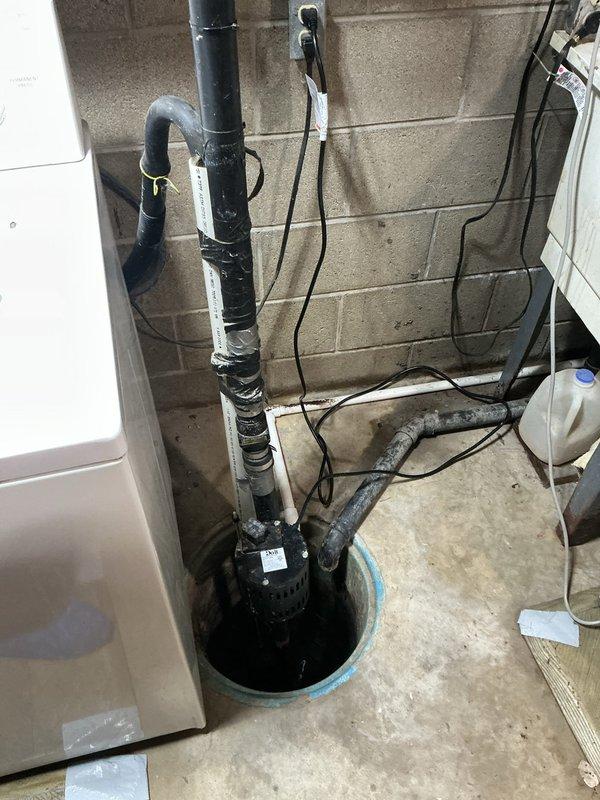 Responded to service call for non-operational sump pump and leaking faucets in kitchen and bathroom. Inspected sump pump system in basement utility area, verifying pump operation, discharge piping integrity, and electrical connections. Examined bathroom faucet fixture with dual-spout chrome design, assessing for leaks at handles, base connections, and supply lines. Documented existing conditions of plumbing fixtures including mineral buildup around drain areas and overall system functionality. Verified sump pump basin installation, submersible pump positioning, and vertical PVC discharge pipe secured to wall with proper fastening. Completed diagnostic assessment of reported issues and documented findings through photographic evidence for service records.