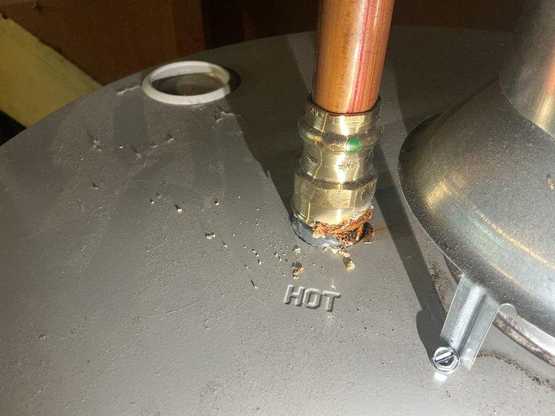 Responded to service call for a two-year-old natural gas water heater with water accumulation in the drain pan. Upon inspection, discovered significant corrosion and oxidation at the hot water outlet connection, with brownish-orange rust deposits accumulated at the copper pipe fitting junction. The corrosion at the brass compression fitting indicated a slow leak that had been depositing water into the safety pan. Documented the condition of the water heater installation, including the expansion tank connections and overall system configuration. The compromised fitting at the hot water outlet required attention to prevent continued water discharge into the drain pan and potential water damage.