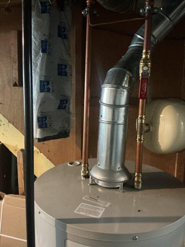 Responded to service call for a two-year-old natural gas water heater with water accumulation in the drain pan. Upon inspection, discovered significant corrosion and oxidation at the hot water outlet connection, with brownish-orange rust deposits accumulated at the copper pipe fitting junction. The corrosion at the brass compression fitting indicated a slow leak that had been depositing water into the safety pan. Documented the condition of the water heater installation, including the expansion tank connections and overall system configuration. The compromised fitting at the hot water outlet required attention to prevent continued water discharge into the drain pan and potential water damage.