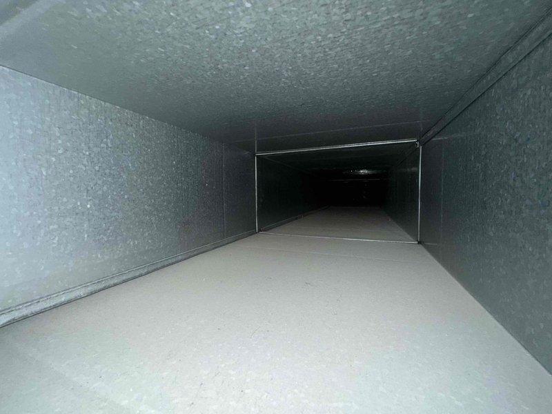 Completed comprehensive duct cleaning service for residential HVAC system. Thoroughly cleaned all accessible ductwork including main trunk lines and branch runs, removing accumulated dust, debris, and particulate matter using professional rotary brush system and high-powered negative air vacuum equipment. Interior duct surfaces, including insulated duct board walls and metal flooring sections, were agitated and extracted to restore proper airflow and indoor air quality. All work performed while insured, and photographic documentation captured showing clean duct interiors with gray fibrous insulation liner and smooth beige flooring post-cleaning.