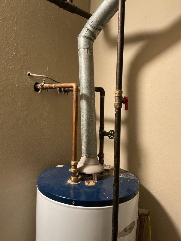 Conducted on-site assessment for 40-gallon upright water heater replacement due to reported water leak from tank. Inspected existing unit with white exterior body and blue top cap, documenting current installation configuration including copper supply lines, brass fittings, pressure relief valve, shut-off valves with red handle, gray insulated piping, and PVC drain connections. Evaluated utility closet installation space with brown tile flooring and assessed all plumbing connections at top and base of unit. Photographed complete water heater setup showing all piping configurations, connection points, Energy Guide label, and manufacturer specifications to prepare replacement estimate. Verified 40-gallon capacity and standard residential installation requirements for accurate quote preparation.