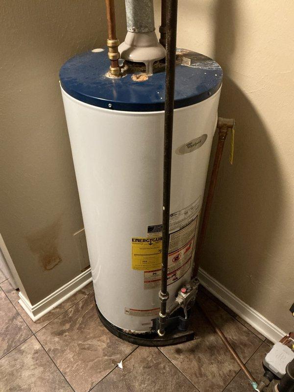 Conducted on-site assessment for 40-gallon upright water heater replacement due to reported water leak from tank. Inspected existing unit with white exterior body and blue top cap, documenting current installation configuration including copper supply lines, brass fittings, pressure relief valve, shut-off valves with red handle, gray insulated piping, and PVC drain connections. Evaluated utility closet installation space with brown tile flooring and assessed all plumbing connections at top and base of unit. Photographed complete water heater setup showing all piping configurations, connection points, Energy Guide label, and manufacturer specifications to prepare replacement estimate. Verified 40-gallon capacity and standard residential installation requirements for accurate quote preparation.