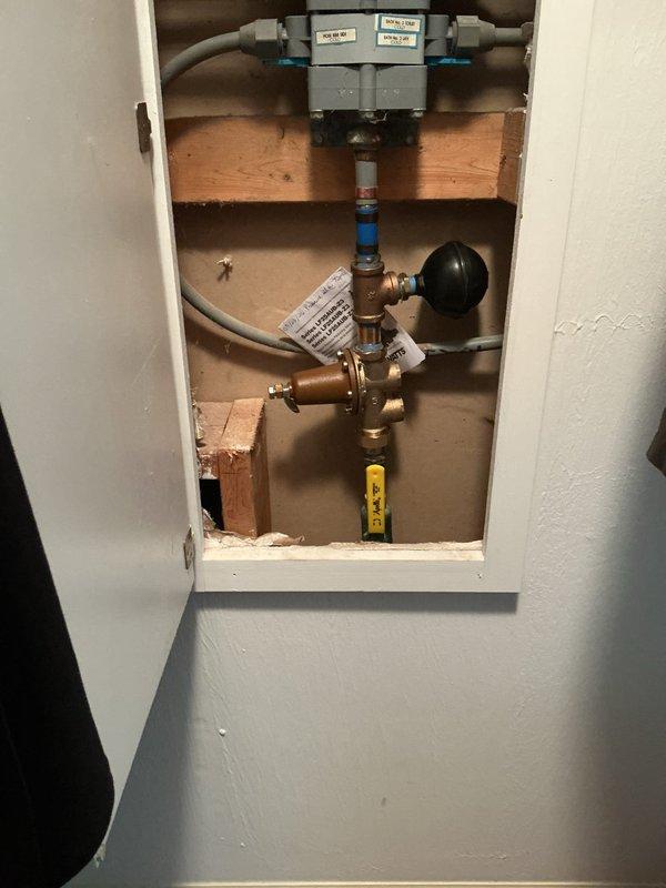 Replaced existing pressure reducing valve (PRV) and installed new 3/4"x3/4"x1/2" tank tee with tankless-style expansion tank to regulate water pressure and accommodate thermal expansion in the system. Work required careful handling due to existing polybutylene 3/4" supply line running to water manifold. Installation included brass fittings, pressure gauge, and black expansion tank mounted within wall cavity access panel, with all components tested and verified operational upon completion.