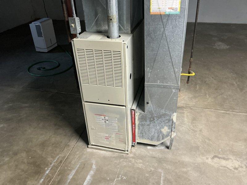 Conducted estimate for replacement of 25-year-old residential furnace system currently still operational. Inspected existing beige cabinet-style furnace unit with horizontal louver ventilation panel, associated galvanized ductwork with diamond-pattern cross-bracing, and cylindrical supply plenum connection. Documented equipment condition, ductwork configuration, and basement installation layout with photographs for replacement proposal preparation.