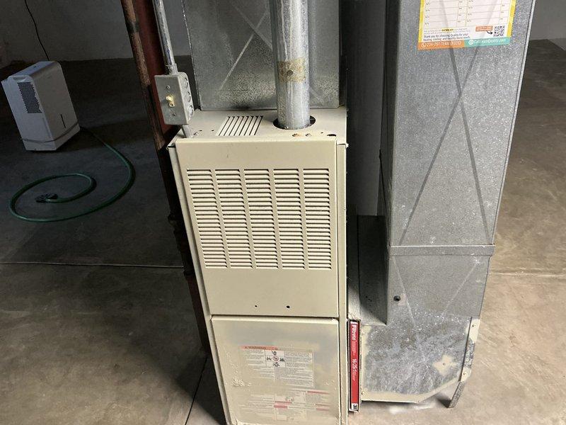 Conducted estimate for replacement of 25-year-old residential furnace system currently still operational. Inspected existing beige cabinet-style furnace unit with horizontal louver ventilation panel, associated galvanized ductwork with diamond-pattern cross-bracing, and cylindrical supply plenum connection. Documented equipment condition, ductwork configuration, and basement installation layout with photographs for replacement proposal preparation.