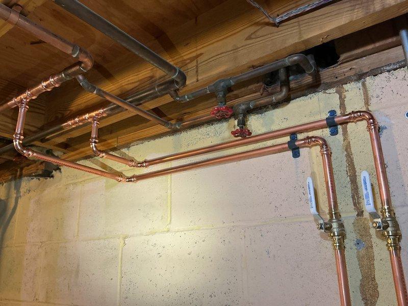 Completed full plumbing installation for new washer and slop sink location in basement utility area. Removed existing copper water supply lines and capped appropriately. Teed off existing 3/4" water lines near water heater and ran new 1/2" copper supply lines to new location, installing hose bibs for washer connection and shut-off valves for deck-mounted faucet along sink wall. Added new straight stop for dishwasher line. Installed drain line from slop sink down to floor, routing across to existing floor drain without trap installation as drain does not connect directly to sewer system. All supply lines secured with proper mounting brackets and fittings tested for leaks upon completion.