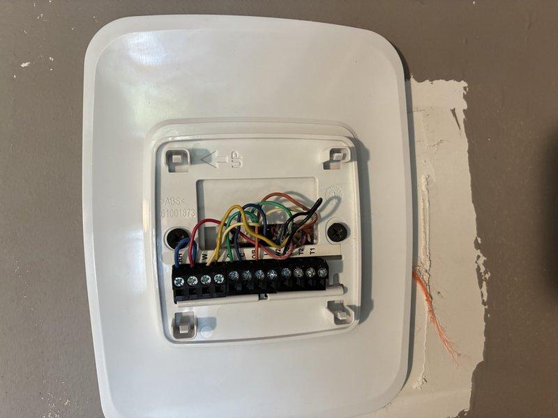 Responded to no cooling call and inspected thermostat at 120 service call location. Found significant corrosion on thermostat wiring terminals and connections, indicating moisture intrusion or age-related deterioration. Documented existing wiring configuration with multiple low-voltage connections (R, Y, G, B, O, C) before removal, noting rust-colored oxidation on wire bundle and terminal block that was preventing proper electrical contact and system communication.