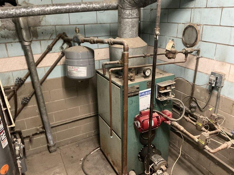 Conducted comprehensive on-site evaluation of existing HVAC system including furnace, air conditioning, and boiler equipment to provide replacement options. Assessed current mechanical room configuration with aging teal-colored boiler featuring mounted expansion tank, red circulation pump, and extensive copper piping showing visible corrosion and wear, along with separate gray furnace unit connected to PVC condensate drainage and metal ductwork, and water heater installation. Documented equipment conditions, measured existing installations, evaluated ductwork and piping infrastructure, and photographed all components to prepare detailed replacement estimate with multiple equipment options for customer consideration.