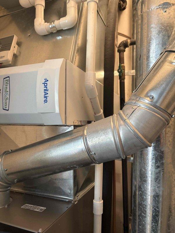 HVAC installation failed initial inspection due to improper condensate line routing from Aprilaire humidifier making contact with flue pipe, creating a safety hazard. Documented code violation with photographic evidence showing PVC condensate drain line positioned too close to exhaust flue in mechanical space. Job placed on hold pending manager approval for corrective action and re-routing of condensate line to maintain proper clearance from high-temperature flue pipe per manufacturer specifications and local building codes.