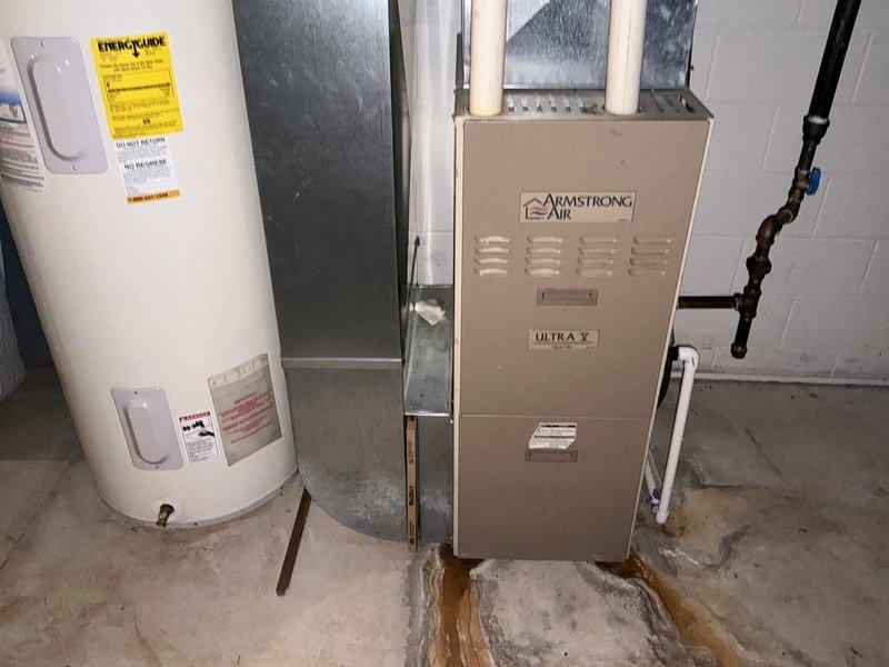 Conducted furnace replacement estimate for Armstrong Air Ultra V unit with reported cracked heat exchanger as identified by previous contractor. Documented existing basement installation including current furnace configuration, ductwork connections, PVC venting system, and surrounding utility equipment including water heater. Noted evidence of previous water damage on concrete floor near equipment area and assessed accessibility for replacement work.