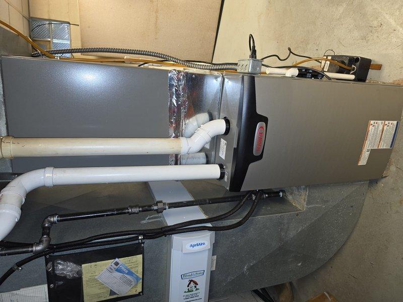 Completed installation of 90% AFUE furnace system in residential utility space. Installed gray metal air handler unit with complete PVC venting system using Schedule 40 pipe, configured condensate drainage lines, and connected refrigerant lines with proper insulation. Integrated Aprilaire humidification system, secured all piping with appropriate mounting hardware, and verified proper clearances per manufacturer specifications.