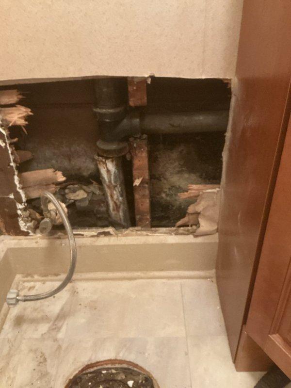 Completed comprehensive plumbing renovation involving removal of deteriorated cast iron piping with significant rust and corrosion. Accessed interior wall cavity to remove and replace compromised drain infrastructure. Replaced toilet flange, lavatory drain assembly, and lavatory faucet in upstairs bathroom. Installed new kitchen faucet. Wall access was required to address aging plumbing components showing heavy oxidation and water damage to surrounding cabinet areas.