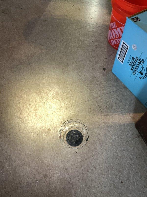 Performed video camera inspection of main drain line to assess condition and identify any blockages or structural issues. Documentation captured showing bathroom floor area with exposed plumbing components including floor drains and flanges, along with utility space drain location where camera access was established for thorough line evaluation.