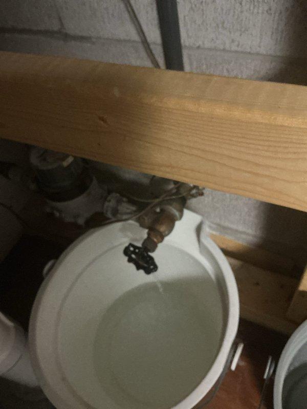 Responded to a basement water valve leak that was continuously dripping approximately one gallon per hour despite being in the closed position. Upon inspection, found a corroded valve with compromised seals causing the persistent leak. Placed collection buckets beneath the failing valve to contain water discharge and assessed the plumbing configuration, which included PVC supply lines and existing shut-off valves in an unfinished basement area with exposed framing and insulation.