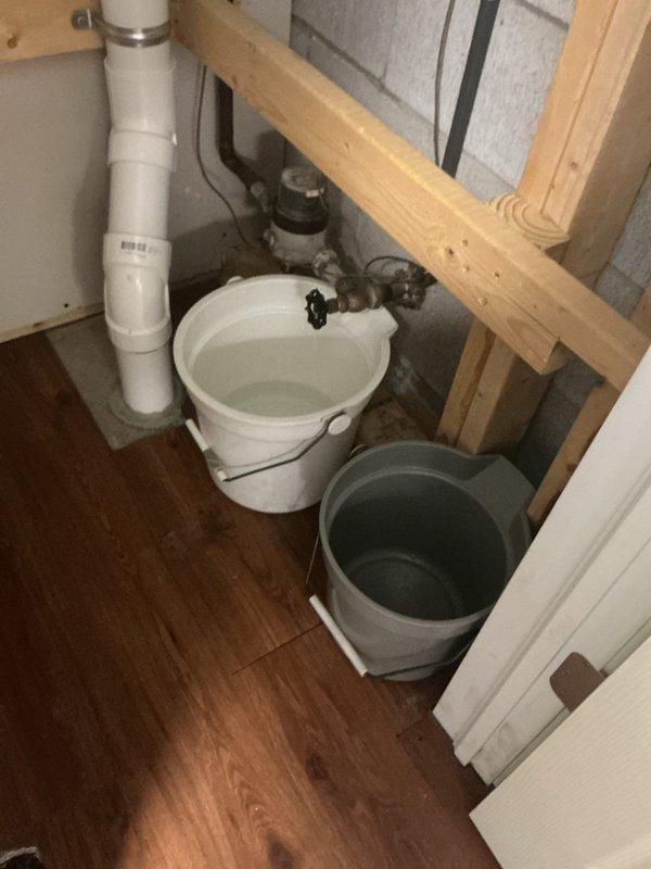 Responded to a basement water valve leak that was continuously dripping approximately one gallon per hour despite being in the closed position. Upon inspection, found a corroded valve with compromised seals causing the persistent leak. Placed collection buckets beneath the failing valve to contain water discharge and assessed the plumbing configuration, which included PVC supply lines and existing shut-off valves in an unfinished basement area with exposed framing and insulation.