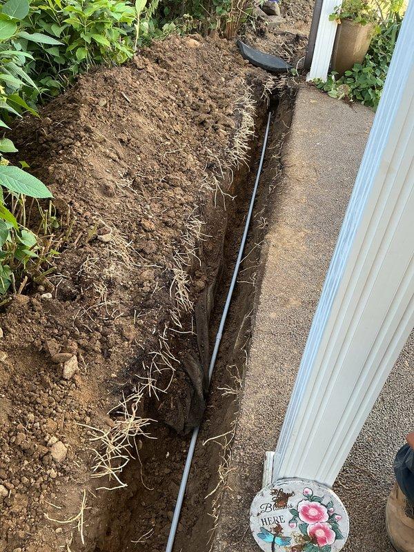 Installed new 20-amp circuit from main panel to back corner of residence, running through 18-inch deep trench to garage man door with complete PVC conduit protection throughout underground run. Corrected existing three-way switch in garage that was previously miswired as a disconnect, removed old conduit at exterior outlet and replaced with new bell box, receptacle, and weatherproof cover. Pulled three-wire cable back to basement laundry room and properly terminated all conductors per code requirements.