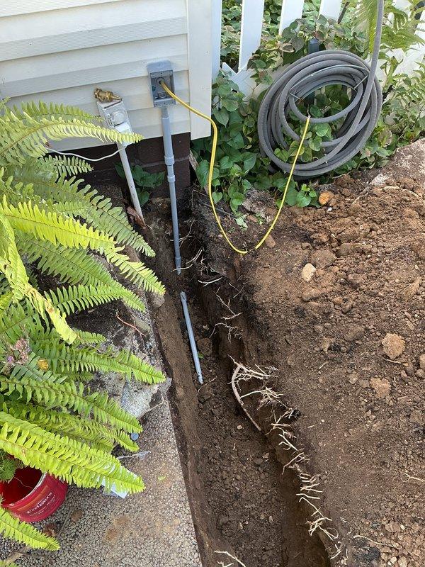 Installed new 20-amp circuit from main panel to back corner of residence, running through 18-inch deep trench to garage man door with complete PVC conduit protection throughout underground run. Corrected existing three-way switch in garage that was previously miswired as a disconnect, removed old conduit at exterior outlet and replaced with new bell box, receptacle, and weatherproof cover. Pulled three-wire cable back to basement laundry room and properly terminated all conductors per code requirements.