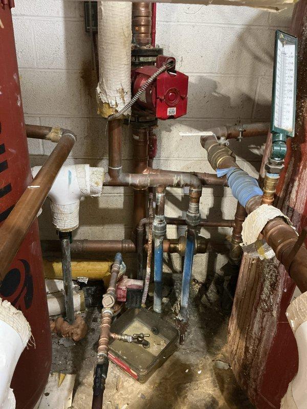 Conducted site assessment of existing tanked water heater system to provide replacement estimates. Inspected current installation including gas-fired water heater unit, associated venting system, gas supply piping with shutoff valve, and connected plumbing infrastructure. Documented existing conditions through photographic records showing water heater, mechanical room plumbing components including circulator pump, copper piping with deteriorated foam insulation, and floor conditions indicating previous moisture exposure. Evaluated installation setup to determine replacement specifications and requirements for two estimate options.