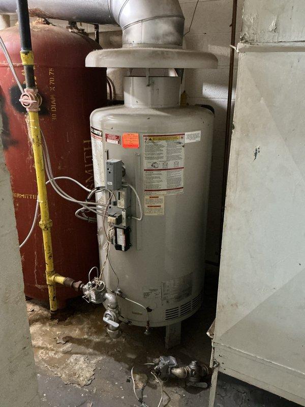 Conducted site assessment of existing tanked water heater system to provide replacement estimates. Inspected current installation including gas-fired water heater unit, associated venting system, gas supply piping with shutoff valve, and connected plumbing infrastructure. Documented existing conditions through photographic records showing water heater, mechanical room plumbing components including circulator pump, copper piping with deteriorated foam insulation, and floor conditions indicating previous moisture exposure. Evaluated installation setup to determine replacement specifications and requirements for two estimate options.